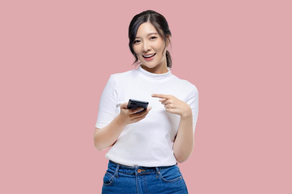 Attractive,Young,Asian,Woman,Pointing,Finger,To,Mobile,Smartphone,On