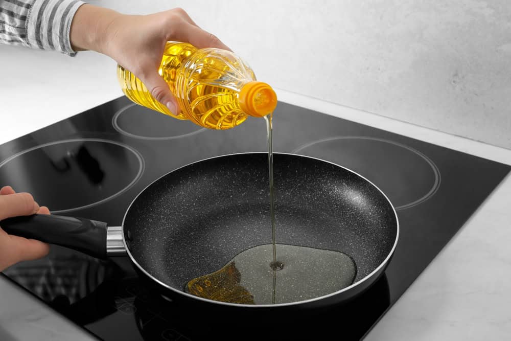 Woman,Pouring,Cooking,Oil,From,Bottle,Into,Frying,Pan,On
